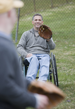 This is a photograph of a man throwing a ball to another man sitting in a wheelchair.