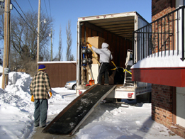 This photograph is of two people unloading a truck using a ramp.