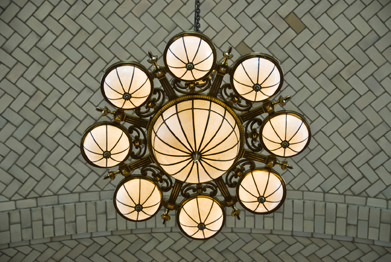 This picture shows a chandelier with a large hemispherical light surrounded by eight smaller hemispherical lights. There are patterned tiles in the background.