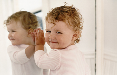 This is a picture of a toddler standing and touching a mirror.