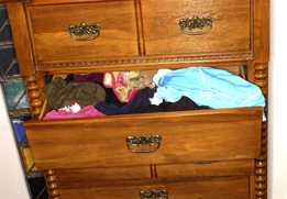 This is a photograph of a chest of drawers with one drawer open and some clothing is shown.