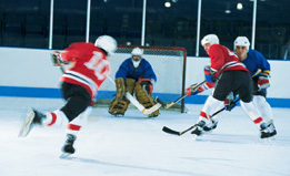 This photograph is of four hockey players with one player taking a shot on goal.