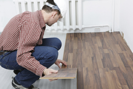 This photograph shows a man installing laminate flooring.