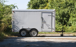 This is a picture of a white utility trailer with green trees in the background.