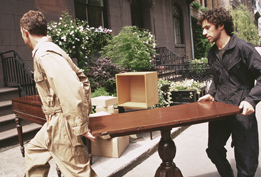 This is a photograph of two men carrying a table up stairs into a house.