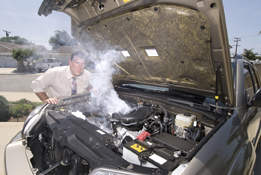 This photograph shows a man looking under the hood of a car that appears to be overheating.