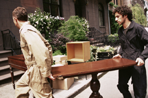 This is a photograph of two men carrying a table up stairs into a house.