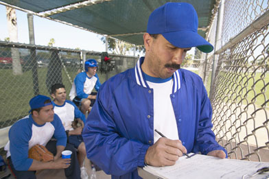 This is a photo of a baseball coach writing on a clipboard in a dugout.