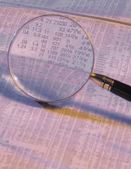 This is a photo of a magnifying glass over a newspaper covered in numbers.