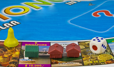 This photo shows a board game playing surface. A green house and two red hotel markers have been placed on the game board. There is also a die and a game token.