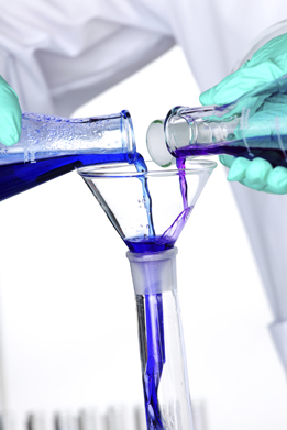 This is a photo of a chemistry experiment. Two solutions from two separate containers are being funneled into one beaker.