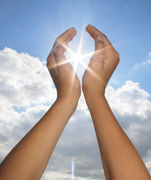 Two hands frame the Sun in a combined blue and cloudy sky.