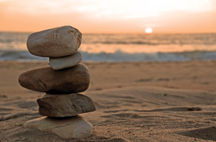A photograph shows rocks balancing on top of one another. A beach and an ocean are shown in the background.