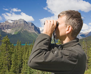 This is a photo of a conservation officer looking through binoculars to survey an alpine ecosystem.