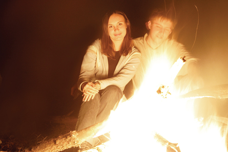 In this photograph, a teenage boy and a teenage girl are sitting at a campfire.