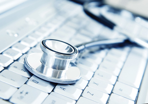 A silver stethoscope is placed on a modern silver keyboard.