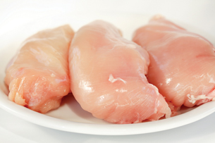 This photo is of three pieces of raw chicken breast on a plate.
