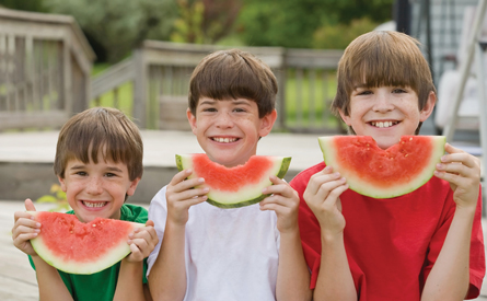 Three boys are eating watermelon in this photo.