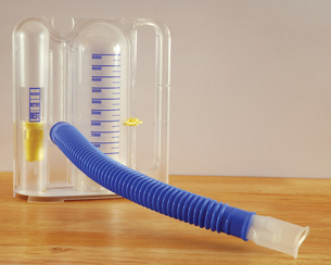 This  photo is of an incentive respirometer. A hose with a mouthpiece extends from a closed tube shape.  Measurements are on the front of the tube. As a person inhales, a lever moves up the side to show what your inhalation capacity is.