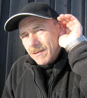 A photograph of a middle-aged man cupping his left ear with his left hand. 