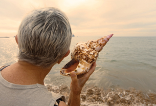Girl holding a conch shell to her ear at the beach.