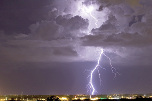 A night photograph shows a bolt of lightning radiating from a cloud and striking the earth over a city.