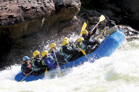 This photograph shows approximately eight people whitewater rafting through rapids on a river. 