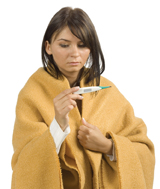 This photograph shows a young woman, who is wrapped in a yellow blanket, checking her temperature with a digital thermometer.