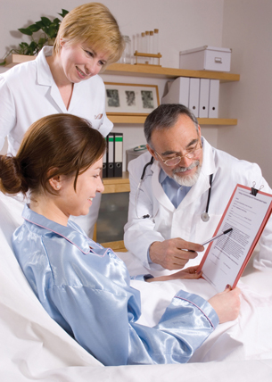 This photograph shows a young woman in a hospital bed. She is looking at a patient consent form with a man in a white doctor’s coat and a woman in a white uniform.