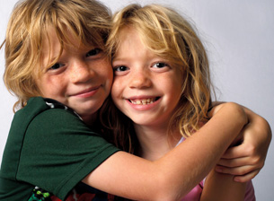 This photo shows a blond boy hugging his twin sister, who is also blond. They appear to be about 7 to 9 years old.