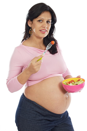 This photograph shows a pregnant woman eating a bowl of fruits and vegetables 