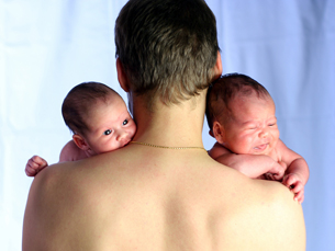 This photograph shows twin babies looking over their father’s shoulders.
