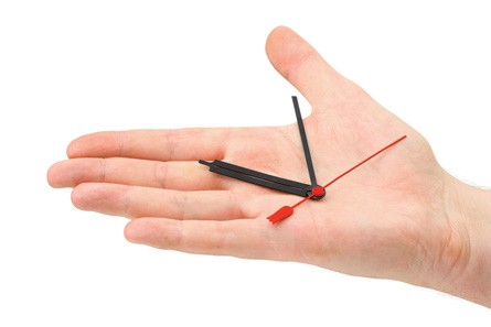 This photo is of an analogue clock that appears to be a part of a person’s hand.