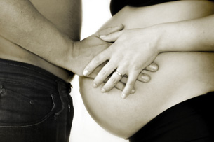The photo shows a man and a woman holding the woman’s very pregnant abdomen.