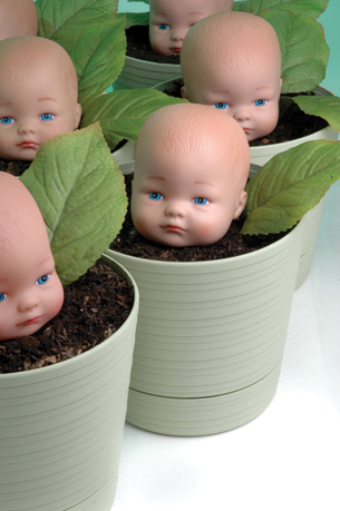 The photo shows identical plastic baby heads growing in plant pots.