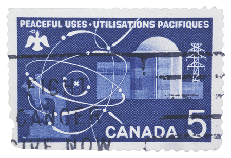 A photograph is shown of a Canadian postage stamp. The stamp contains diagrams of the outside of a nuclear power plant and of a high voltage transmission tower. In the upper- left corner of the stamp is a drawing of a white dove carrying an olive branch in its beak. The title above the dove states “Peaceful Uses”.