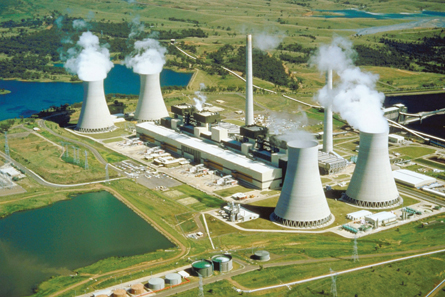 A picture of a nuclear power plant is viewed from an airplane. Four large cooling towers are shown. At the top of each cooling tower is a large steam cloud.