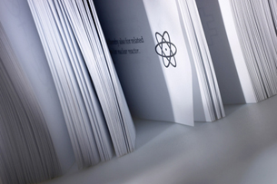 A photograph shows the pages of a report. On the cover of the report is a symbol showing a representation of an atom nucleus surrounded by three ellipses. This symbol is often used to represent nuclear energy.