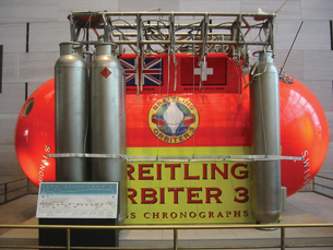 A photograph shows the crew compartment of the Breitling Orbiter 3, a high altitude balloon. The compartment is an oval-shaped capsule with long pressurized gas cylinders vertically positioned along the side of the capsule.