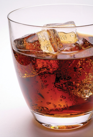 A photograph shows a colourless drinking glass containing a light brown liquid. Within the liquid are many ice cubes and small spherical bubbles.