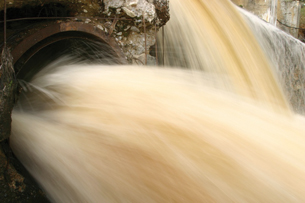 A photograph of water being released from a large pipe into a stream.