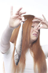 Photograph of a young woman holding a fish in one hand and her nose with her other hand.