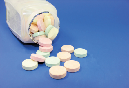 A photograph of multicoloured antacid tablets on a table next to an open pill container.