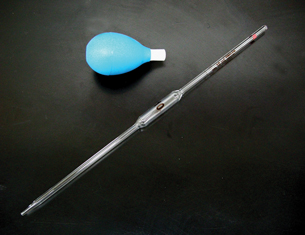 A volumetric pipette and bulb. The pipette is a long thin glass tube with an oval bulge in its middle. The bulb is a compressible rubber object with a plastic cap to fit over the end of the pipette.