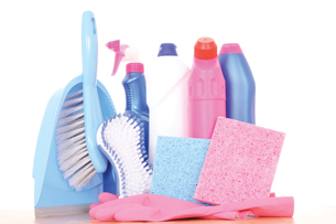 A photograph of various cleaning supplies. Shown are a handbroom and dustpan, a scrub brush, rubber gloves, a sponge, and three bottles of different cleaning products. 