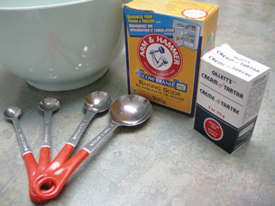 A photograph shows a mixing bowl, four measuring spoons, a box of baking soda, and a small box of cream of tartar.