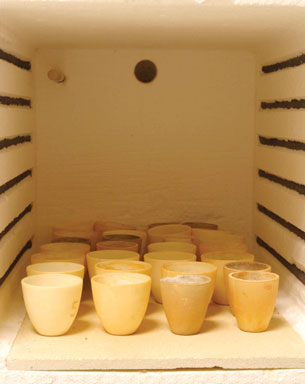 A photograph of the interior of an oven in a chemistry laboratory. Along the bottom shelf of the oven are many small clay crucibles.