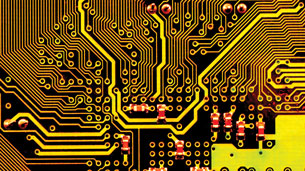 A photograph of a circuit board for a computer. The surface of the circuit board has many small holes. From the small holes are thin lines of copper metal across the circuit board. There are many thin lines arranged closely together, but not touching.