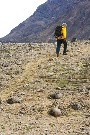 A photograph shows a hiker walking along a rocky trail in a valley surrounded by mountains.