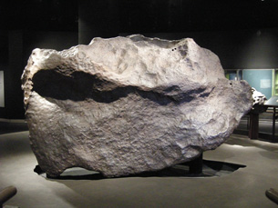 A photograph shows a very large meteorite. The meteorite looks like a large boulder and has a grey exterior.